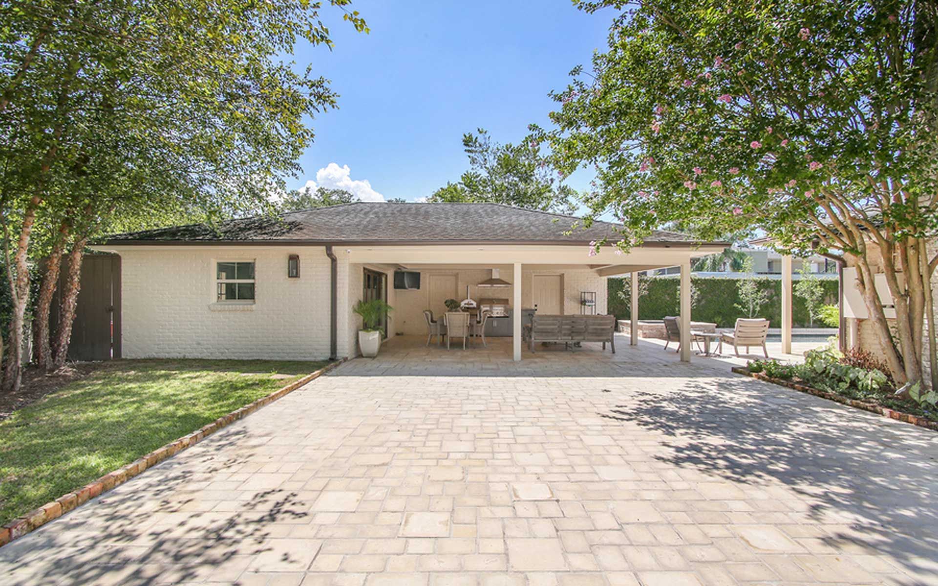 A white house with a covered patio and a driveway leading to it.