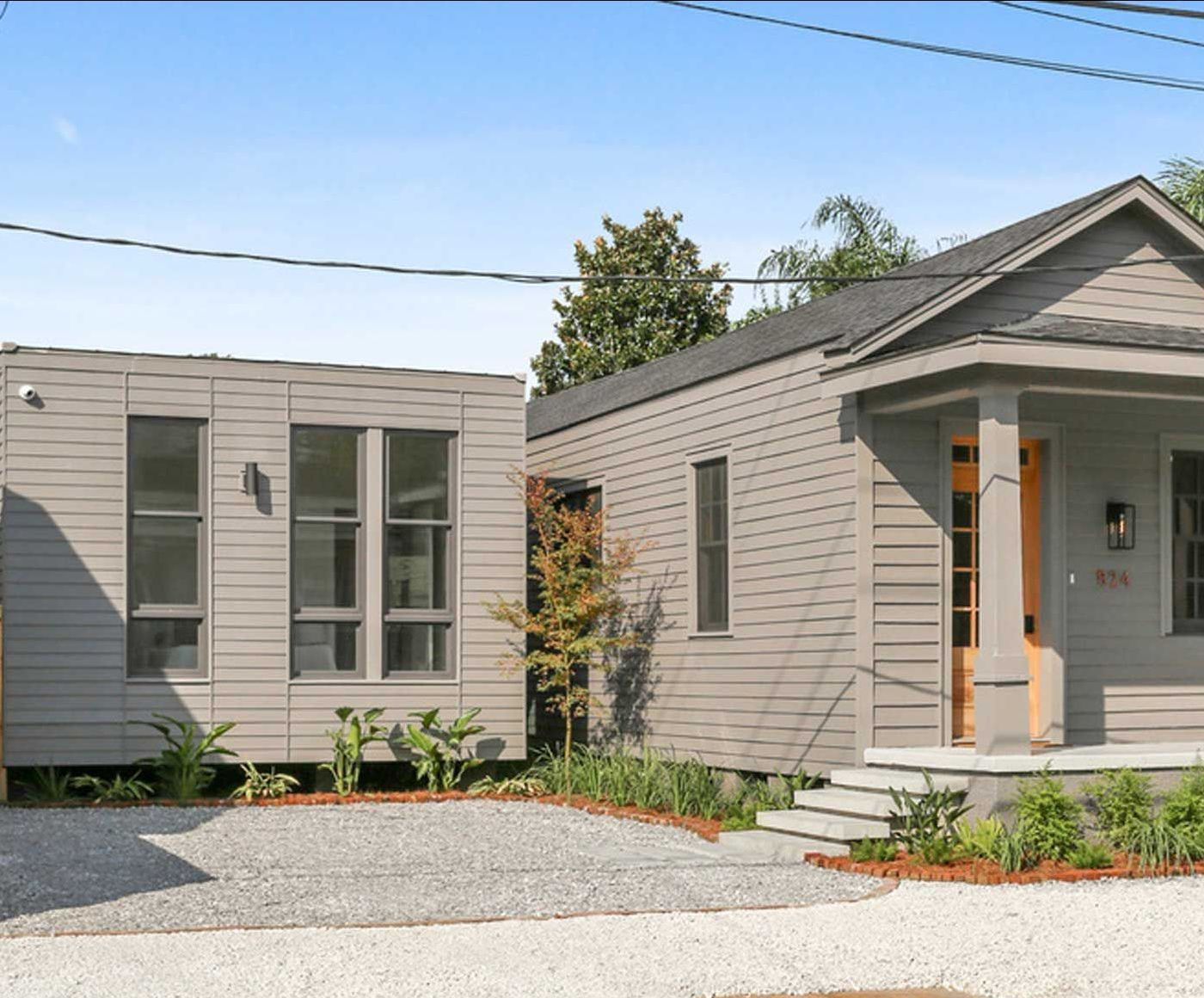 A small house with a lot of windows is sitting next to a larger house.
