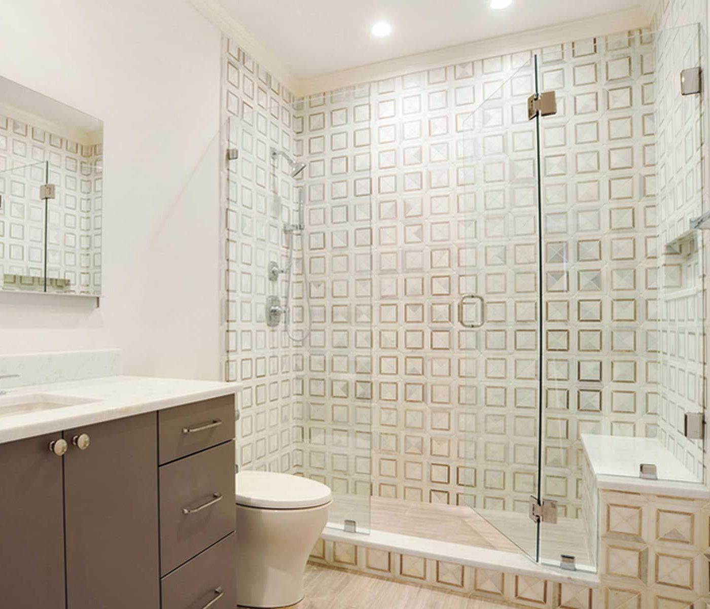 Modern bathroom with patterned tile shower, glass door, toilet, gray vanity.