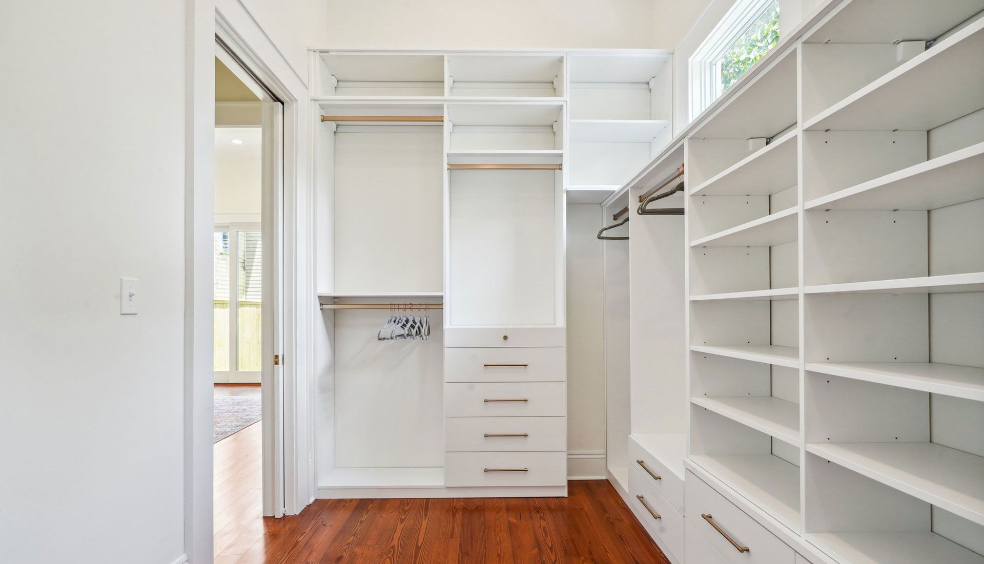 White walk-in closet with shelves, drawers, and hanging rods; wooden floor.