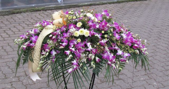 Una vivace composizione floreale funebre con orchidee viola e fiori bianchi