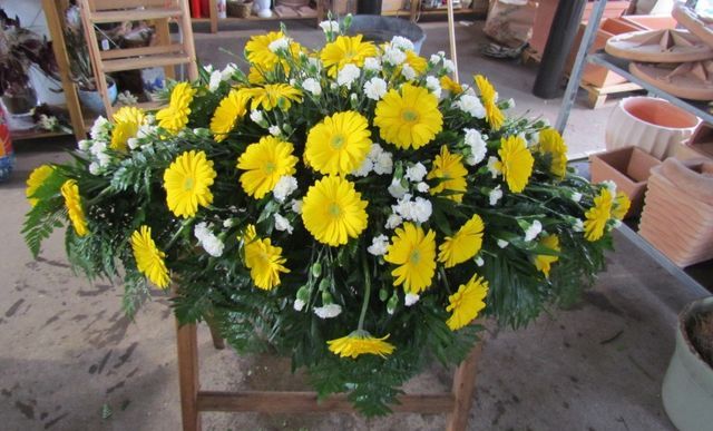 Una vivace composizione floreale funebre con gerbere gialle e garofani bianchi su un supporto di legno.