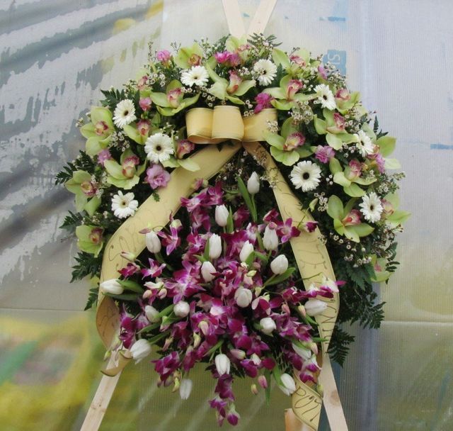 Una corona funebre su un supporto di legno, composta da orchidee cymbidium verdi