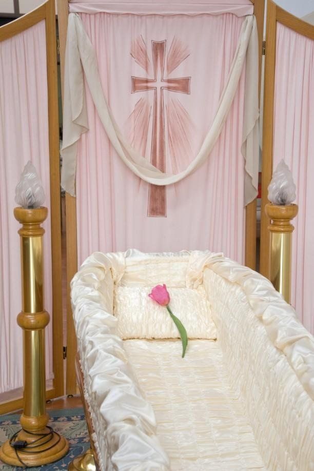 Una bara aperta con fodera in seta color crema e un tulipano rosa sul cuscino