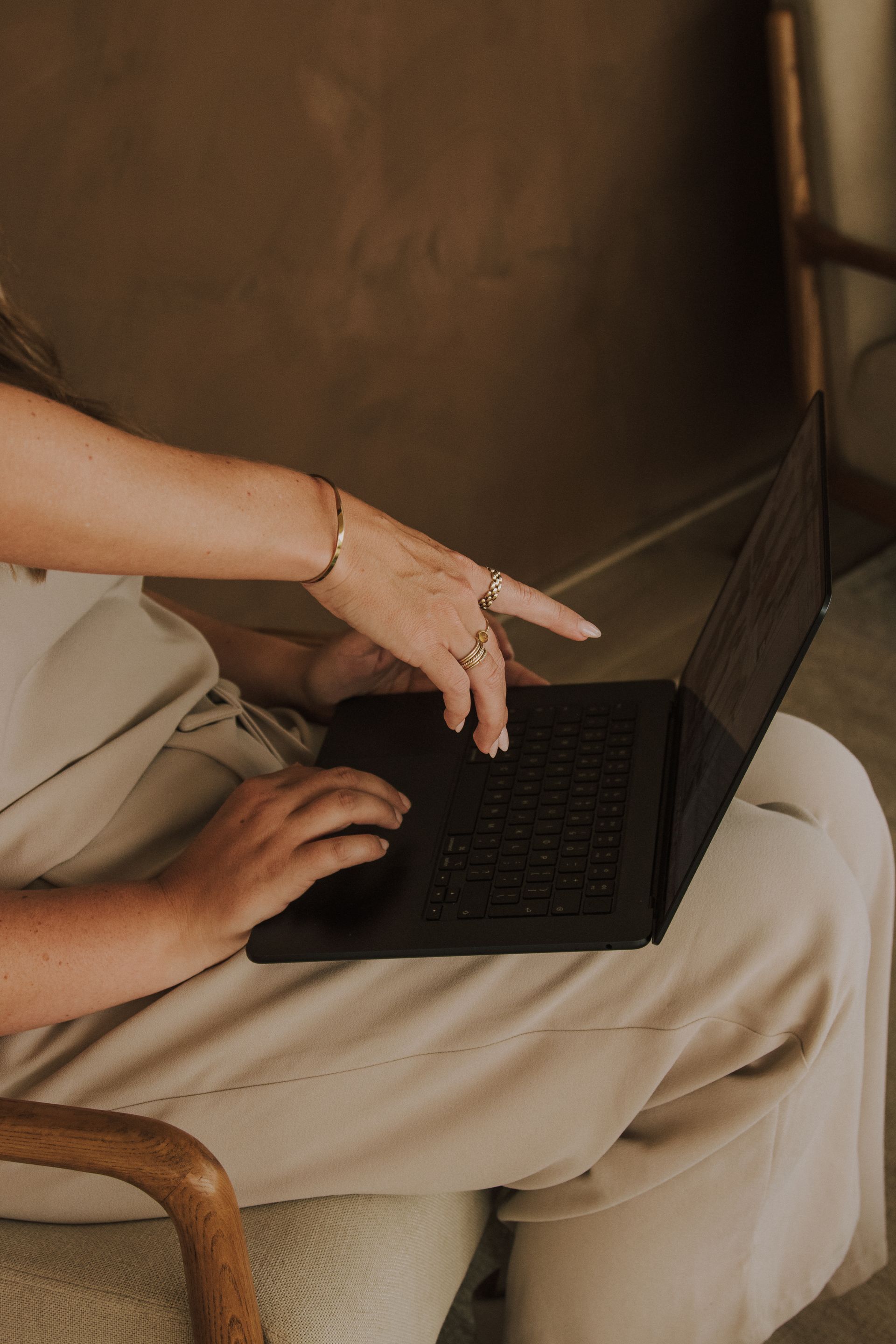 Handen die een laptop op iemands schoot gebruiken, waarbij één hand naar het scherm wijst.