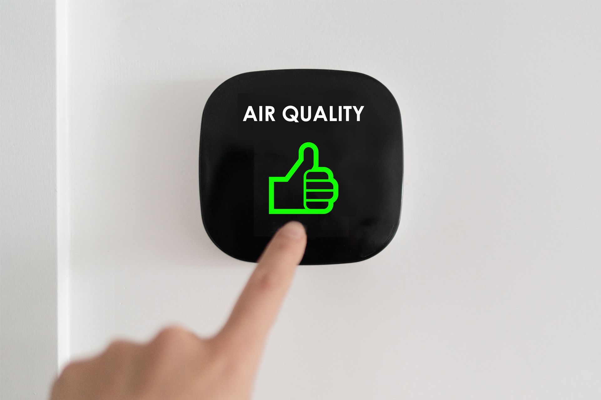 Hand touching a wall-mounted air quality sensor with a glowing green thumbs-up, indicating good air quality.