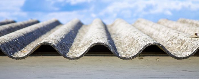 Close-up of wavy, gray roofing material against a blue sky with clouds.