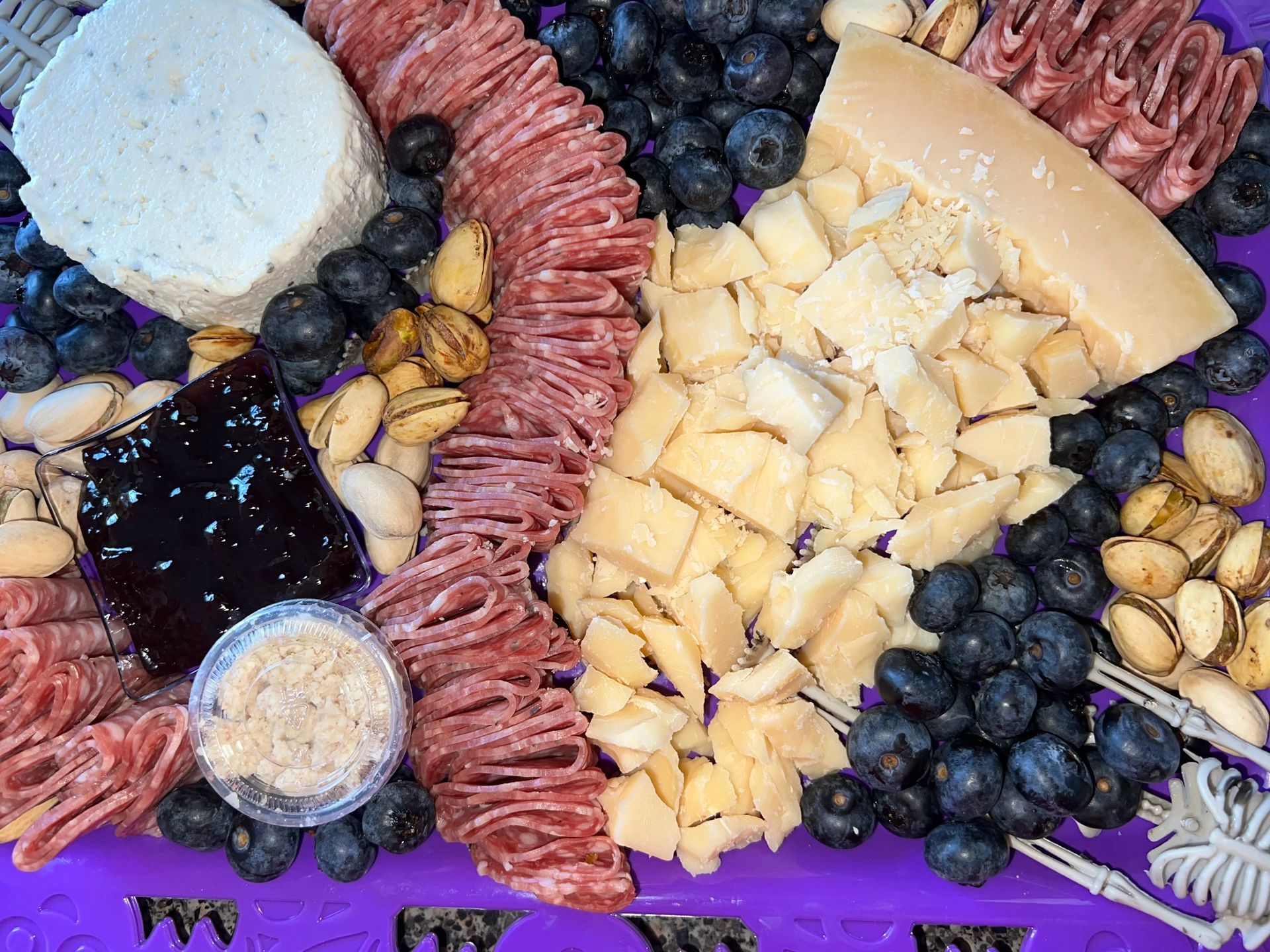 Cheese board with sliced cheeses, nuts, olives, blueberries, jam, and crackers arranged on a platter