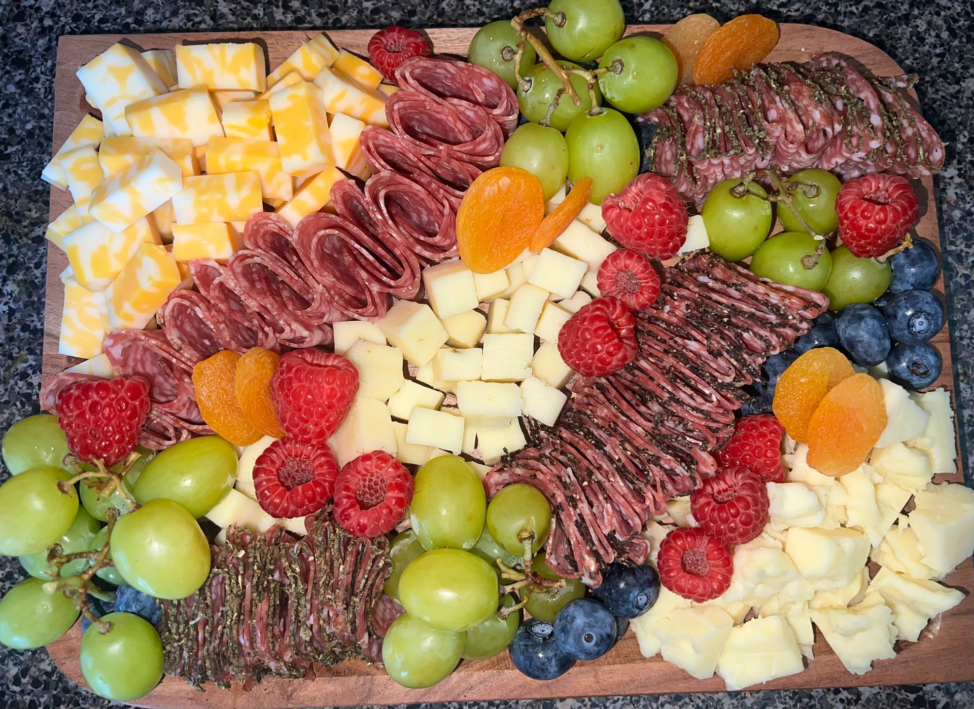 Charcuterie board with cheeses, meats, grapes, berries, and crackers arranged on a platter