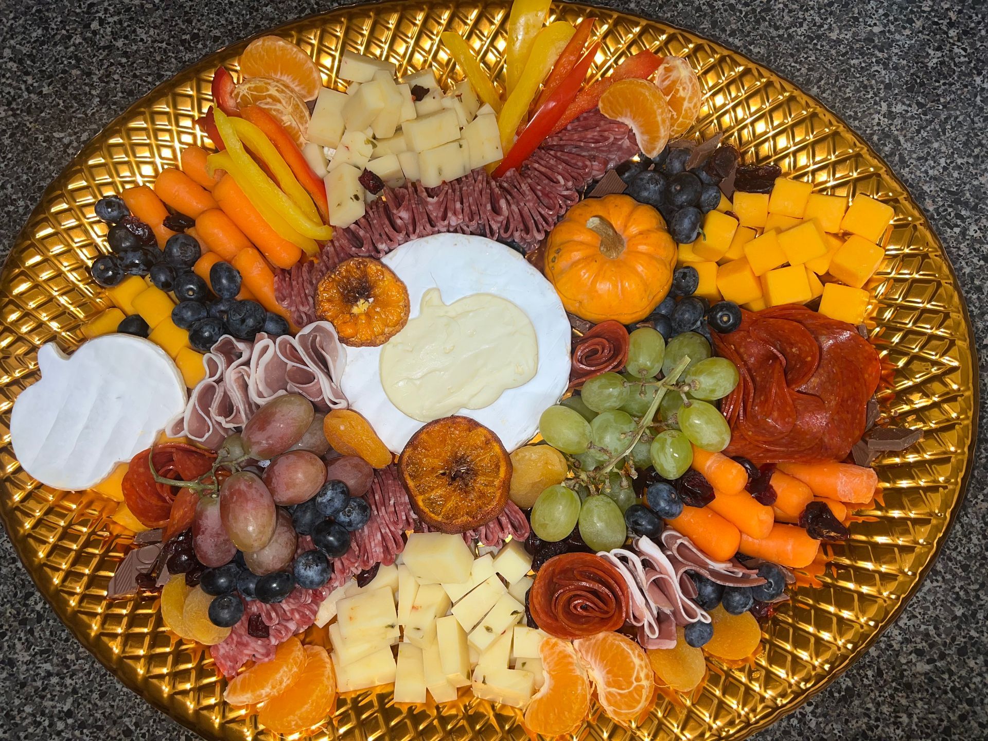 Assorted fruits, cheeses, and snacks arranged on a gold serving platter.