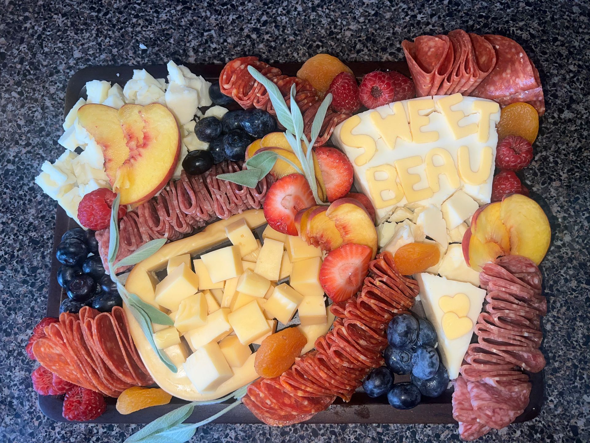 Fruit and cheese charcuterie board with berries, peach slices, and yellow “SWEET” cutouts