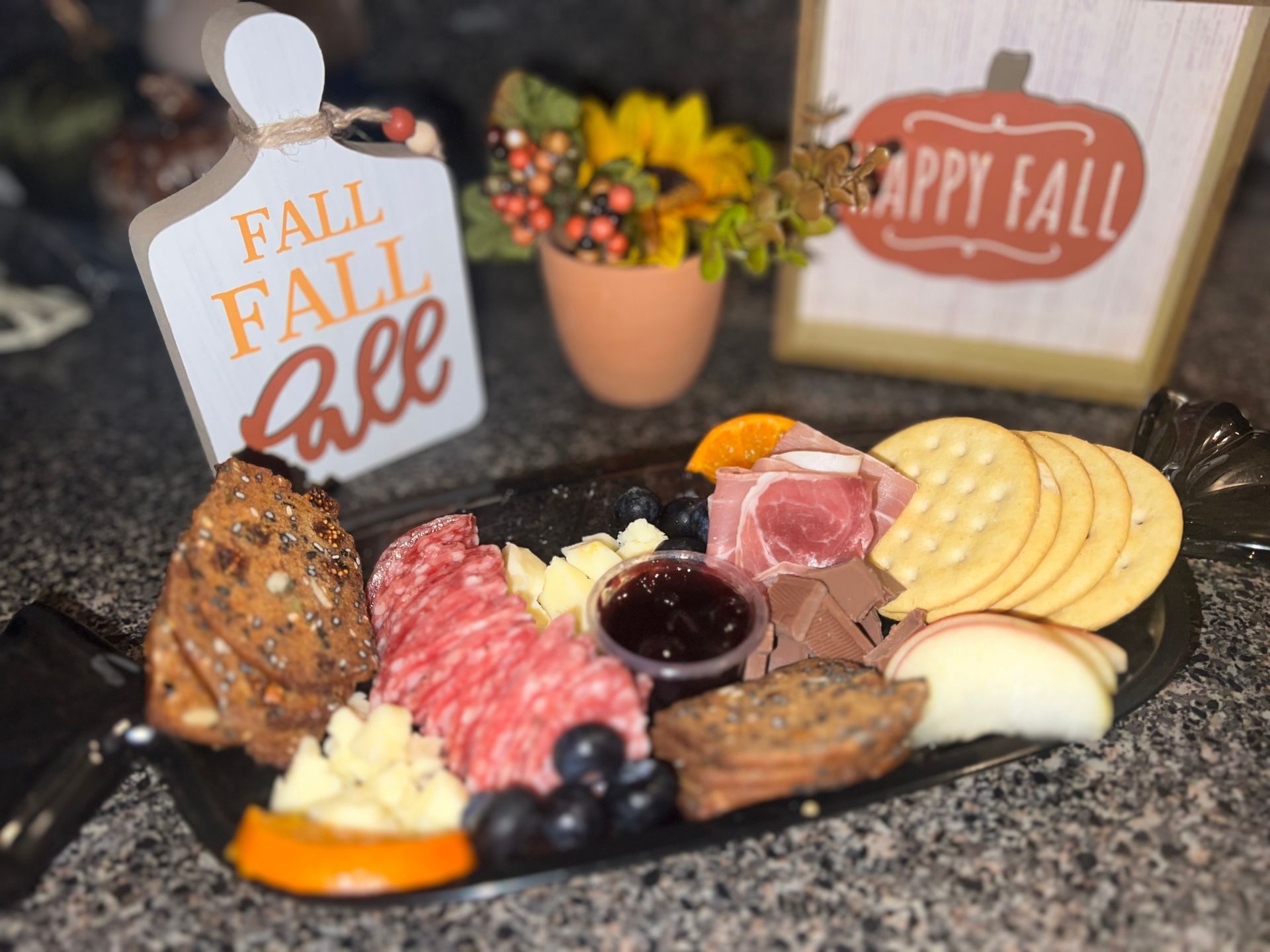 Fall-themed charcuterie board with meats, cheeses, fruit, and fall decorations on a countertop