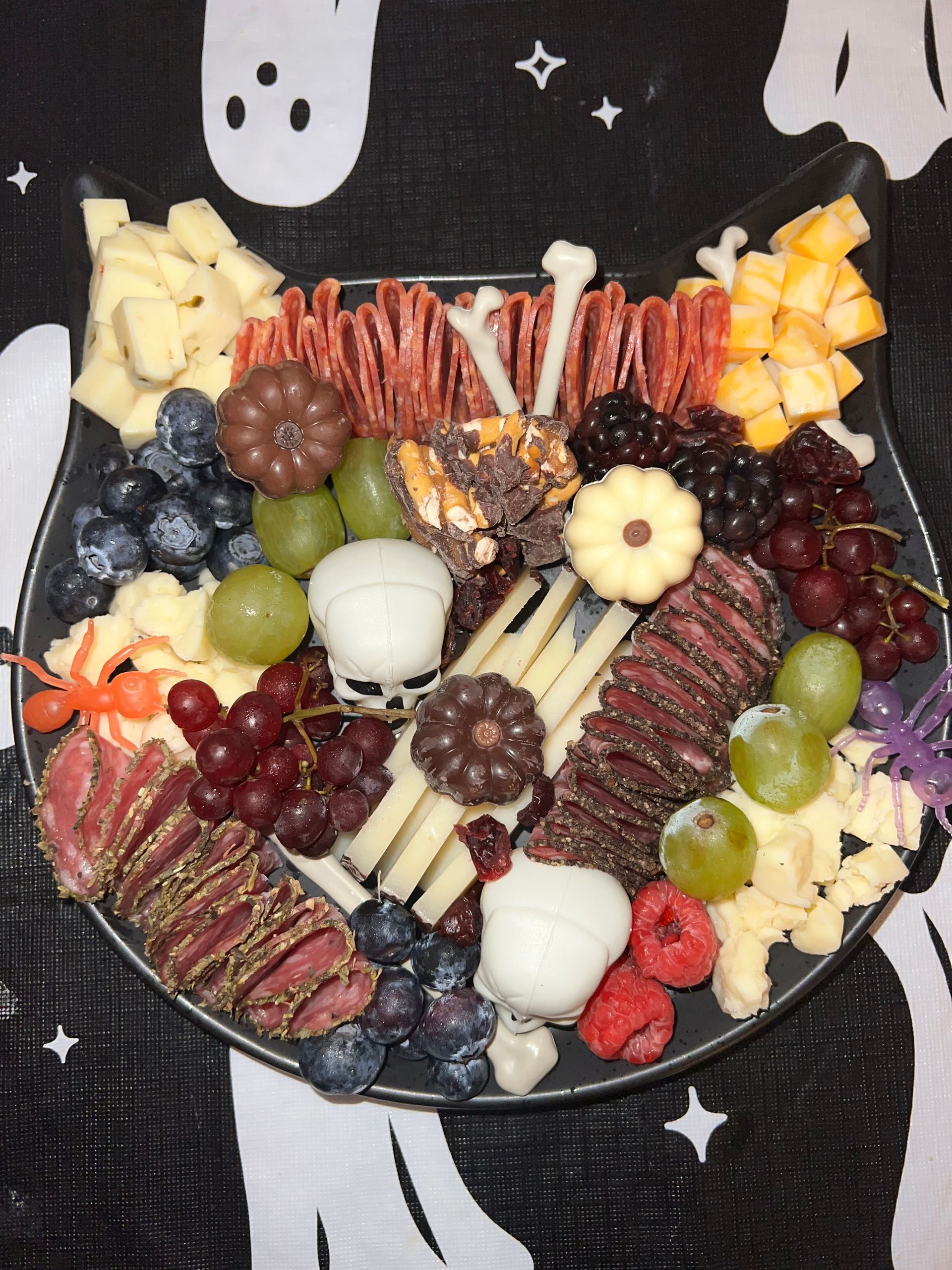 Charcuterie board with assorted cheeses, meats, grapes, berries, and crackers on a dark patterned tablecloth