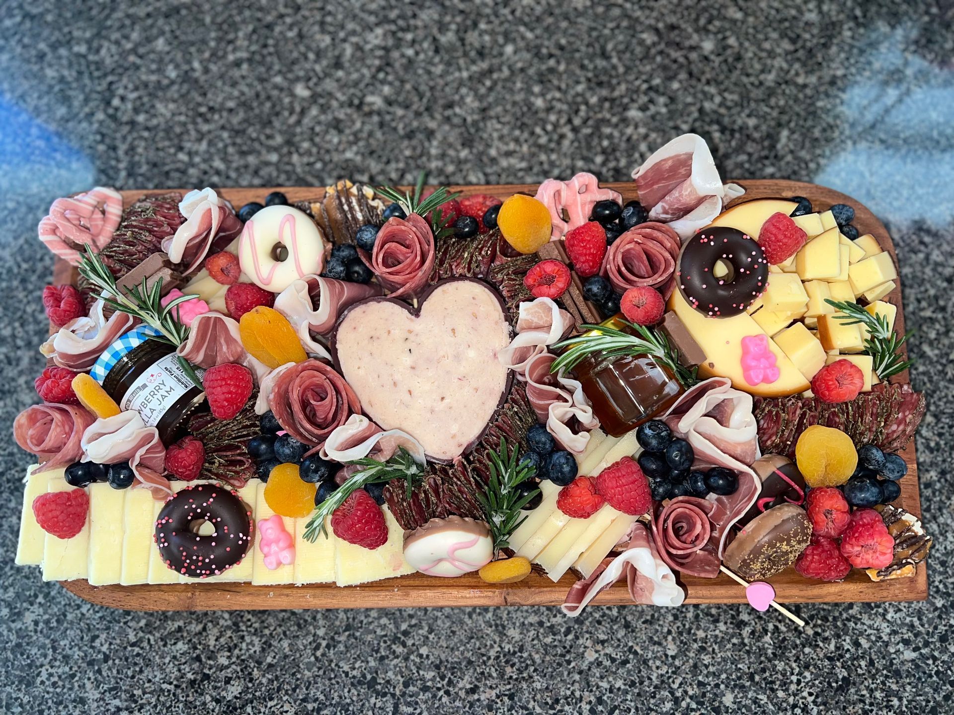 Heart-shaped dessert platter with donuts, cookies, fruit, chocolates, and pink roses on a tray