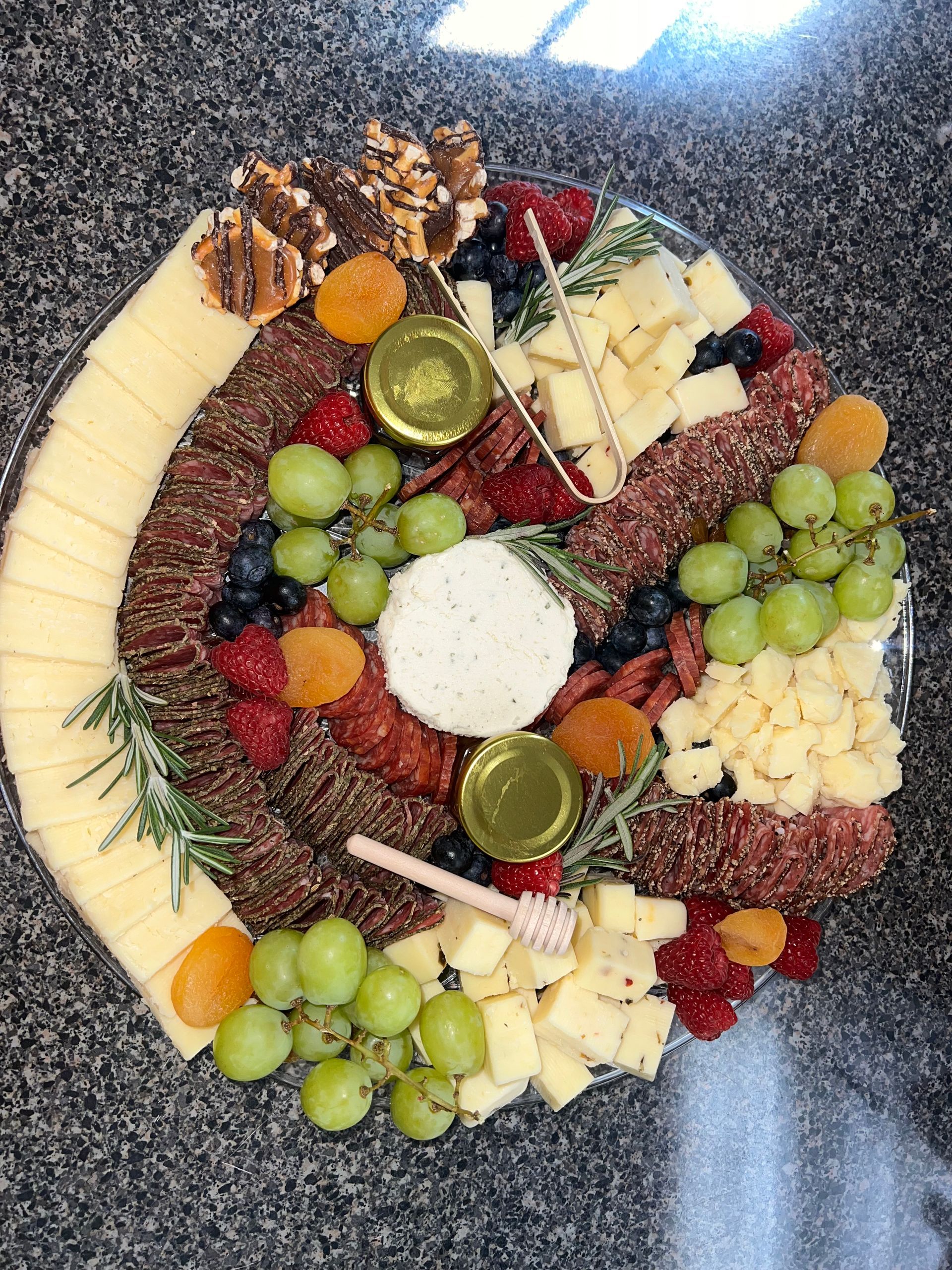 Charcuterie board with grapes, berries, cheese, crackers, nuts, and sliced fruit on a round platter