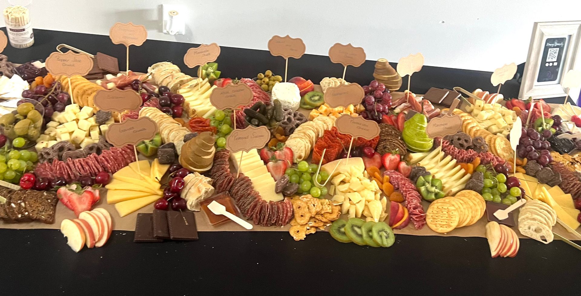 Colorful fruit and cheese grazing table with crackers, nuts, and berries on a black tablecloth