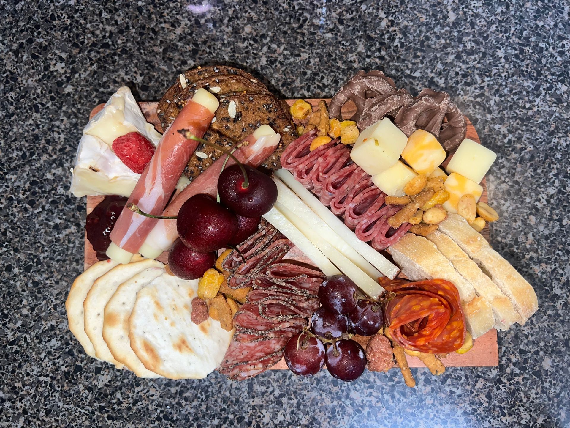 Charcuterie board with sliced meats, cheese, grapes, crackers, and dried fruit on a dark countertop
