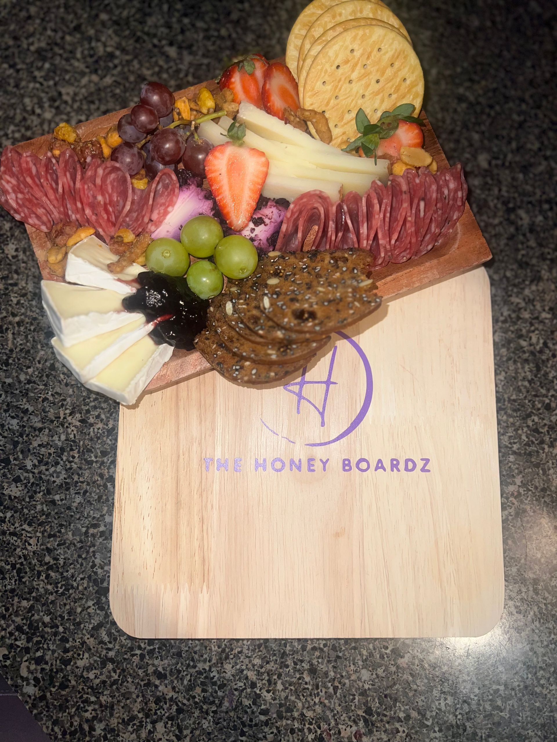 Charcuterie board with meats, cheeses, crackers, grapes, strawberries, and chocolates on a wooden board