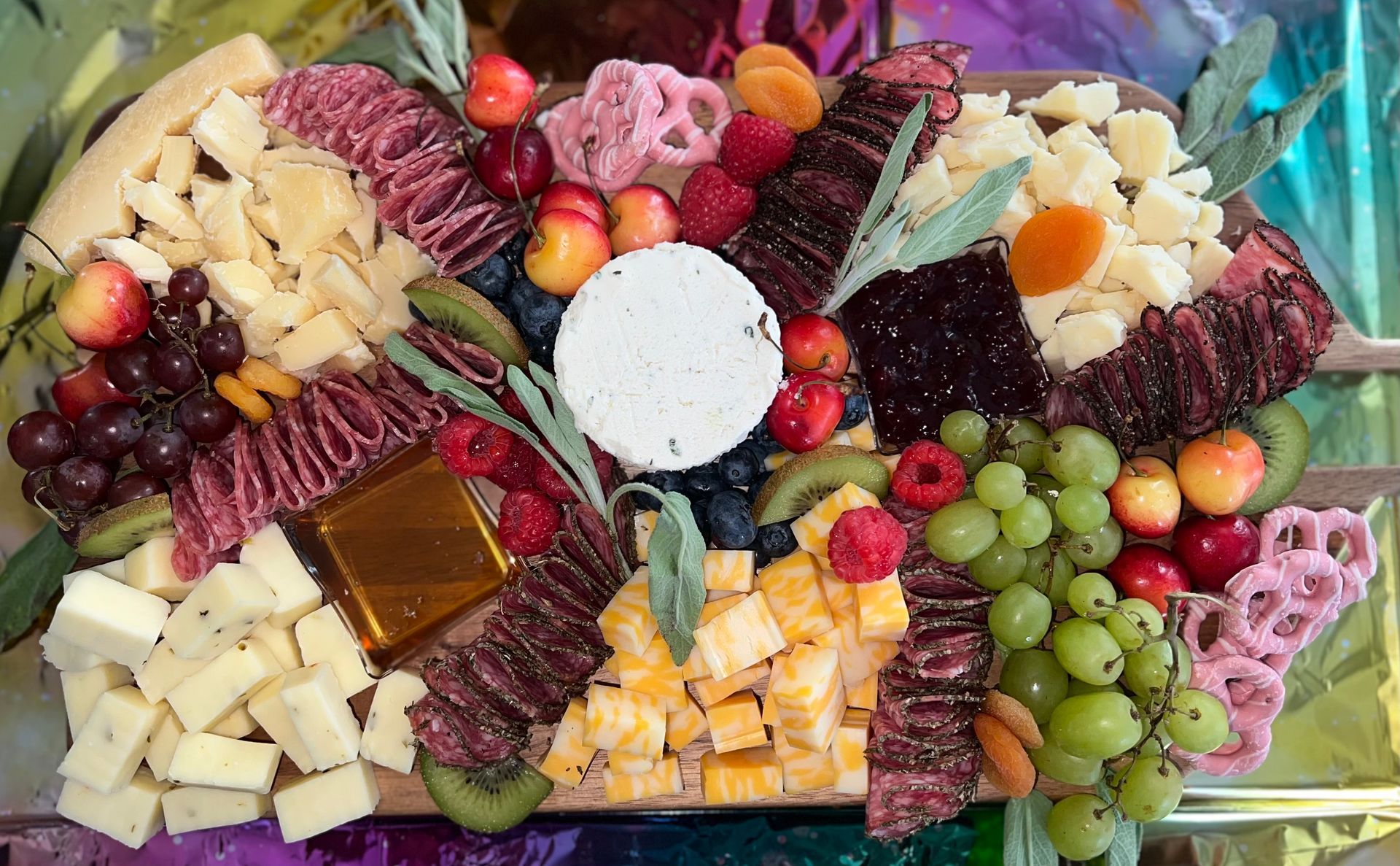 Colorful charcuterie board with cheeses, grapes, crackers, fruit, and a white dip in the center