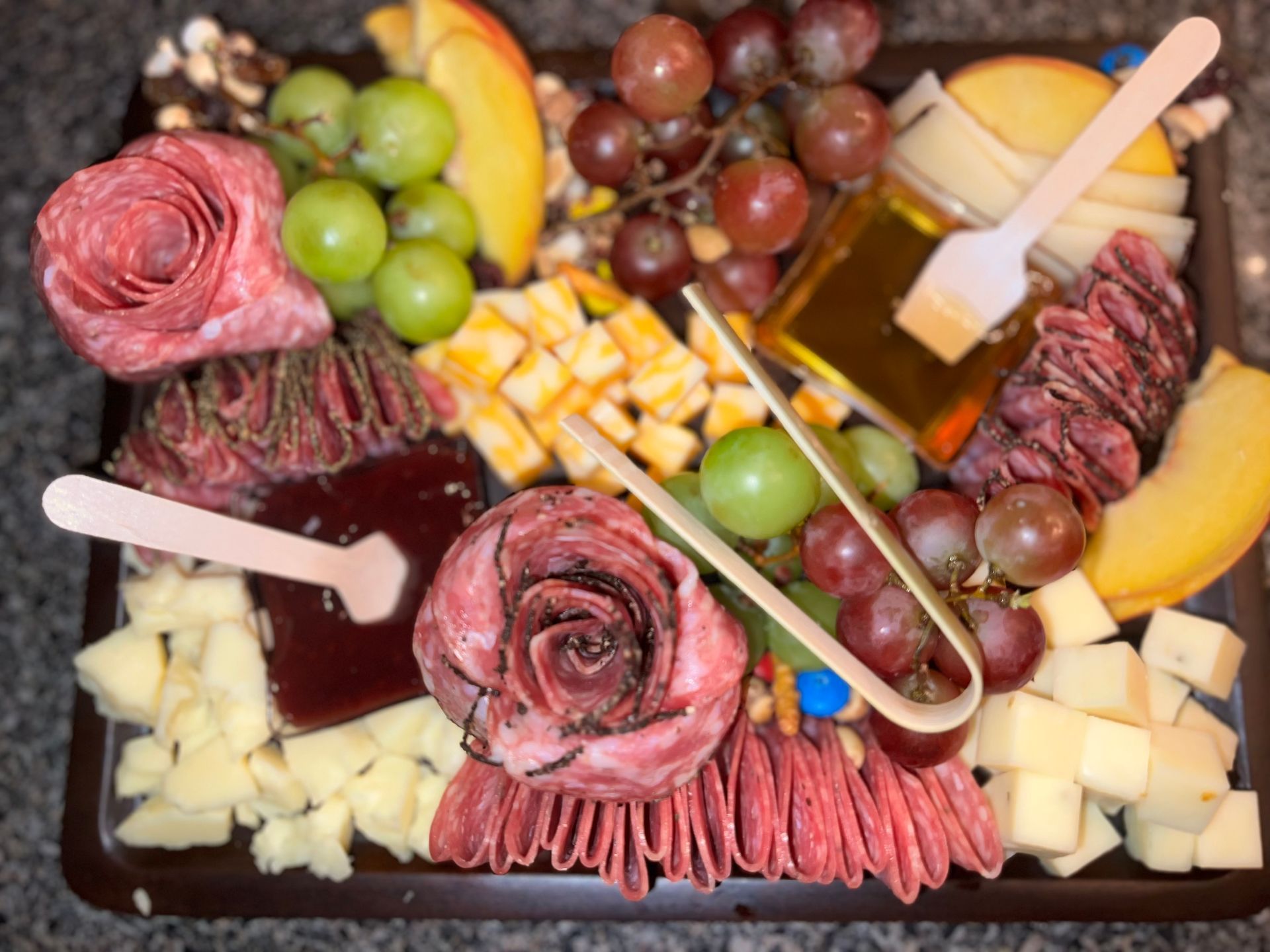 Charcuterie board with meats, cheeses, grapes, and fruit, topped with honey and cheese cubes