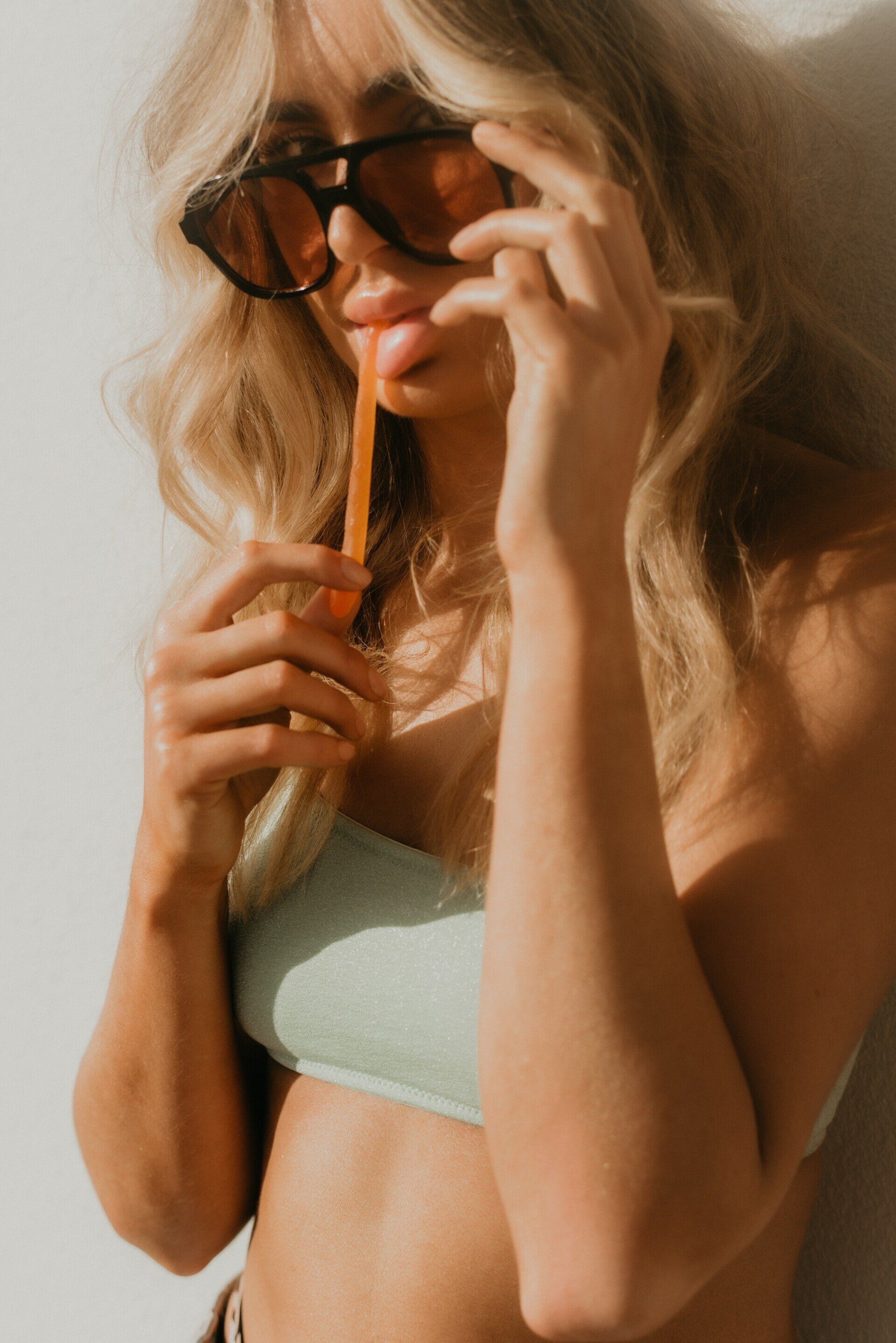 A woman in a bikini and sunglasses is drinking from a straw.