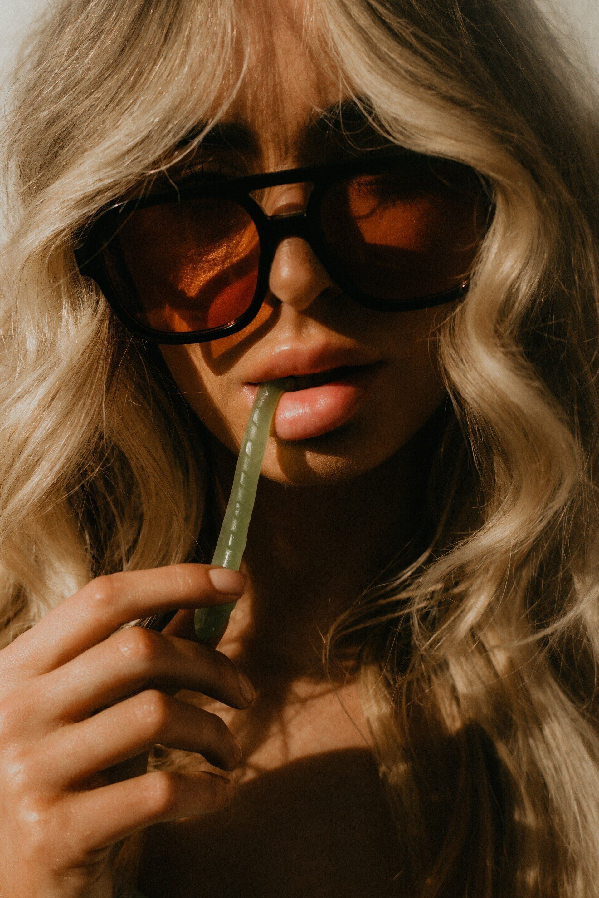A woman wearing sunglasses is drinking through a straw.
