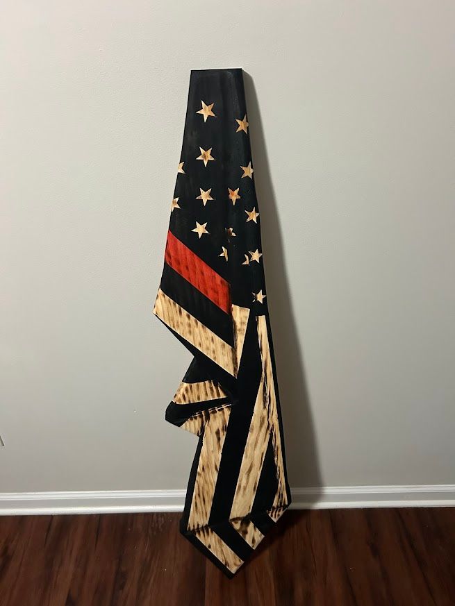 American flag with a red stripe and black field, leaning against a gray wall.