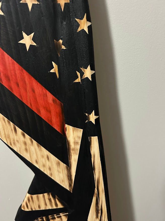 American flag with a red stripe and black field, leaning against a gray wall.