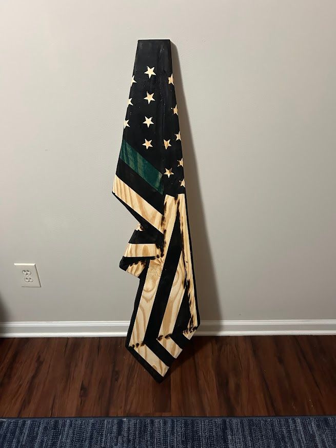 Wooden, distressed American flag with a green stripe hanging on a gray wall.