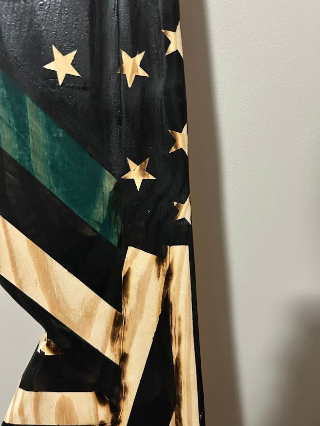 Wooden, distressed American flag with a green stripe hanging on a gray wall.
