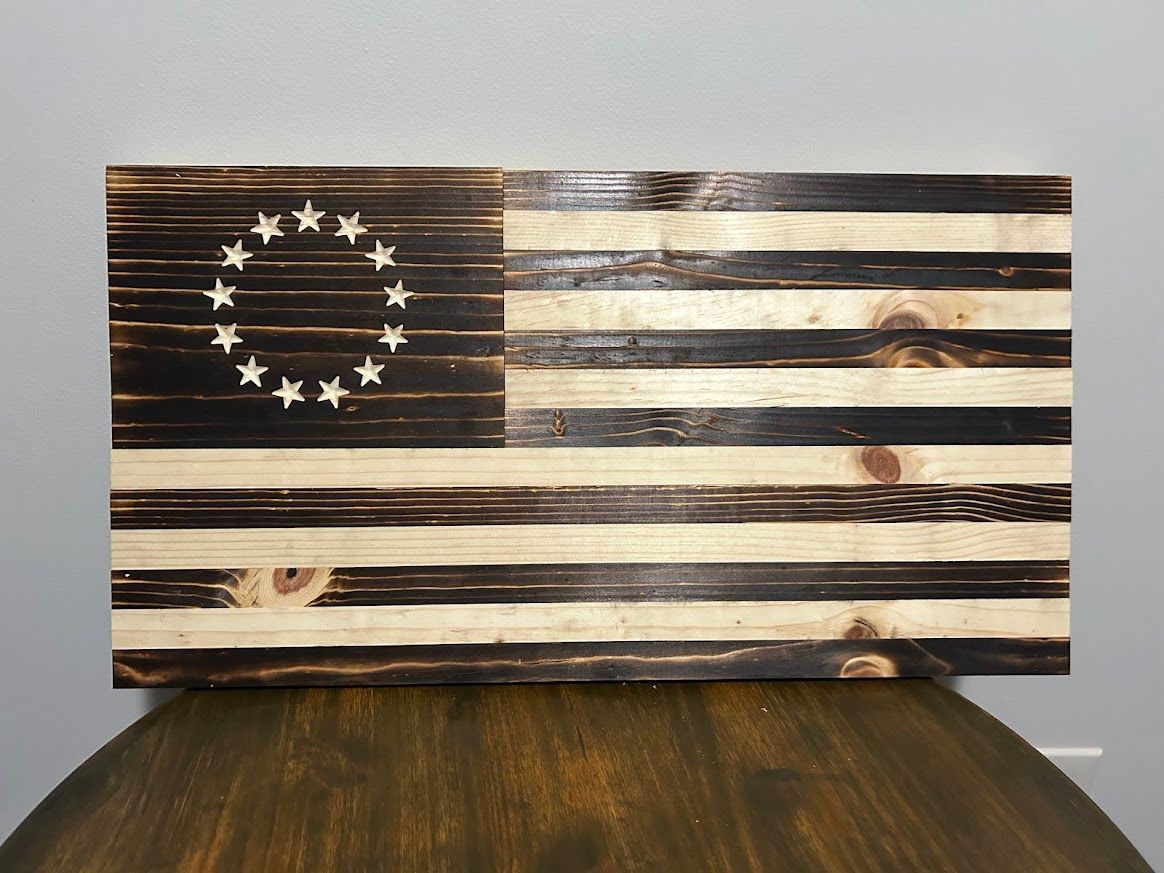 Wooden, rustic Betsy Ross flag. Black charred stripes, white stars in circle, mounted on a wall.