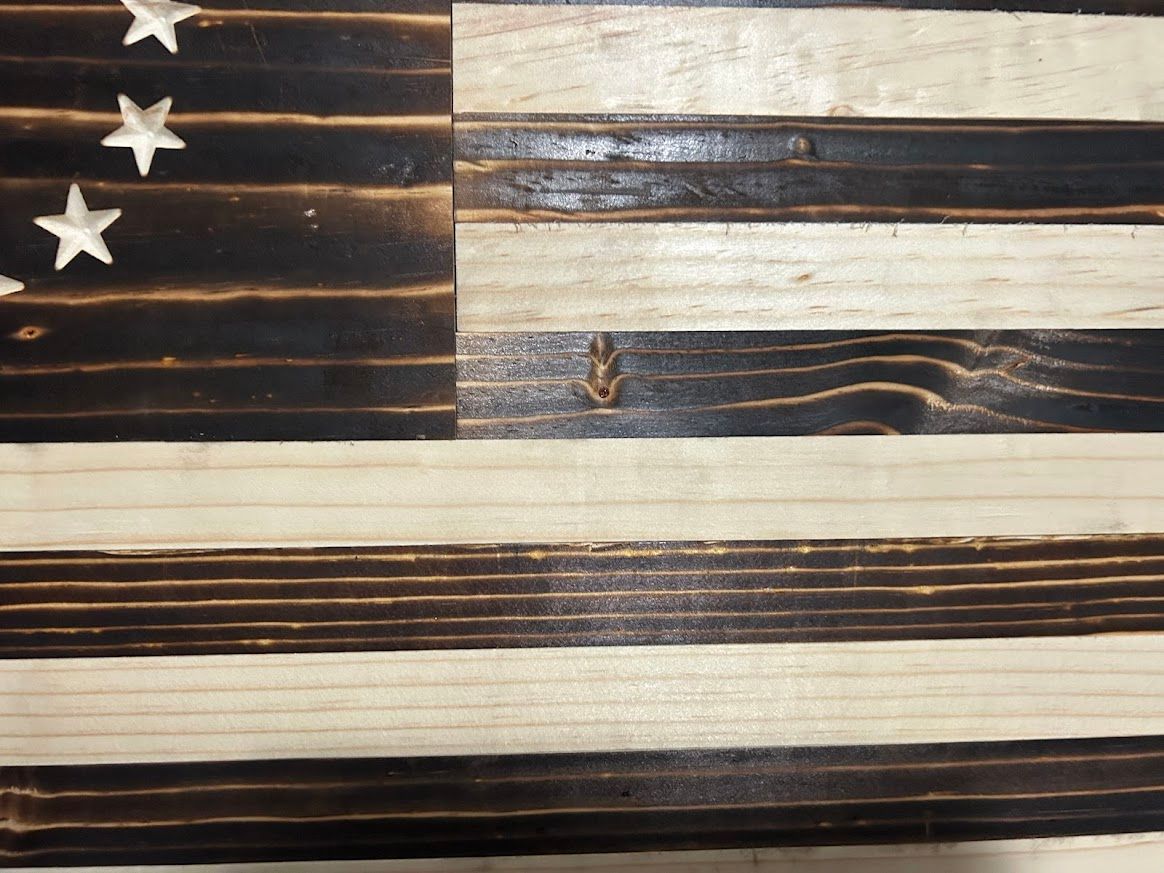 Wooden, rustic Betsy Ross flag. Black charred stripes, white stars in circle, mounted on a wall.