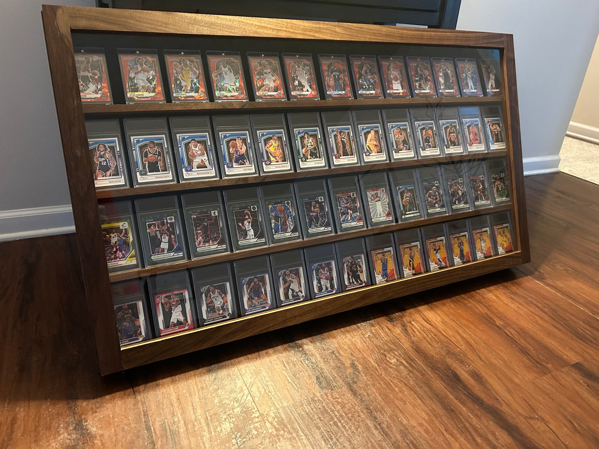 Wooden display case with multiple rows of trading cards, on a wood floor.