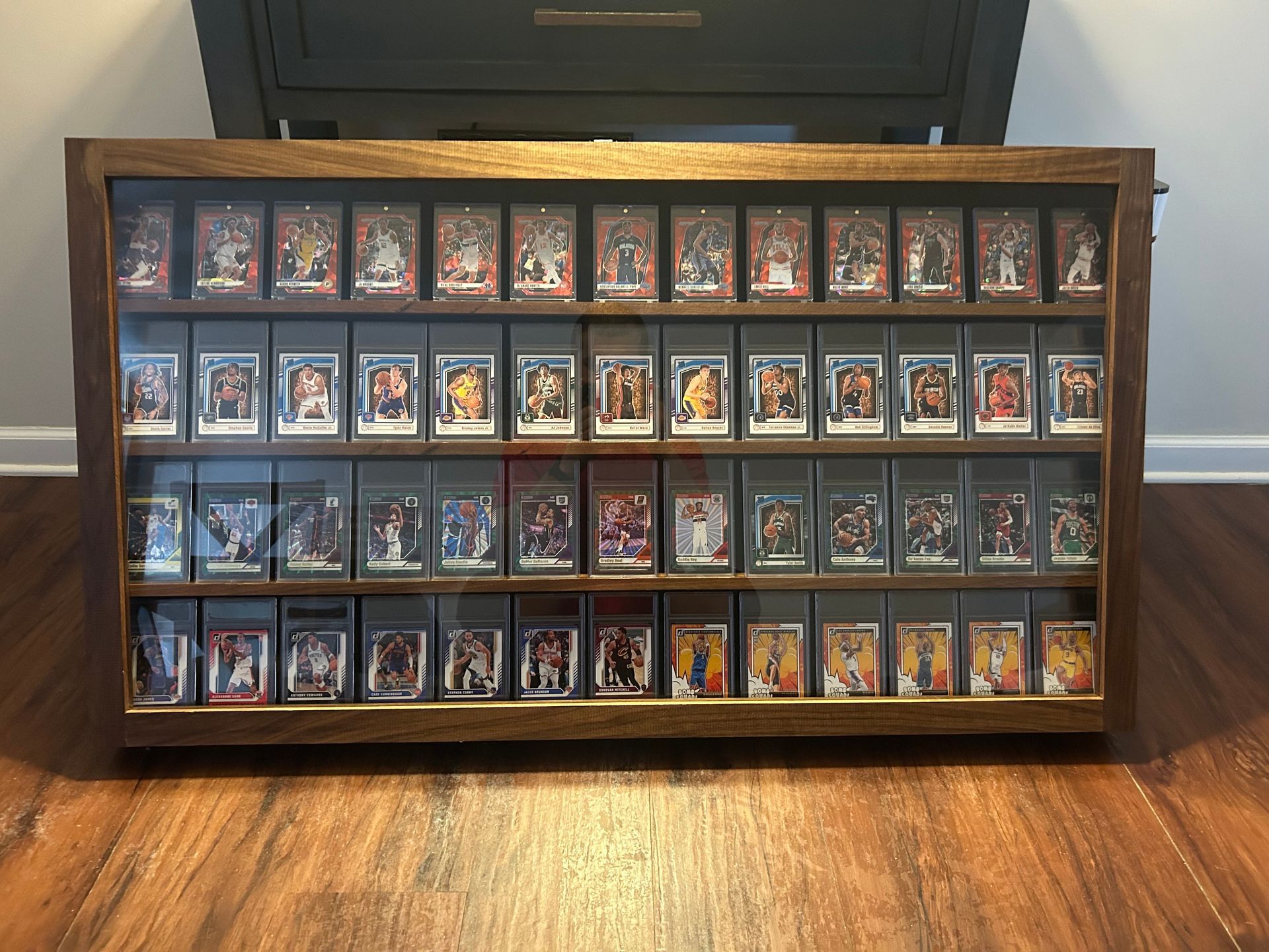 Wooden display case with multiple rows of sports trading cards on a wooden floor.