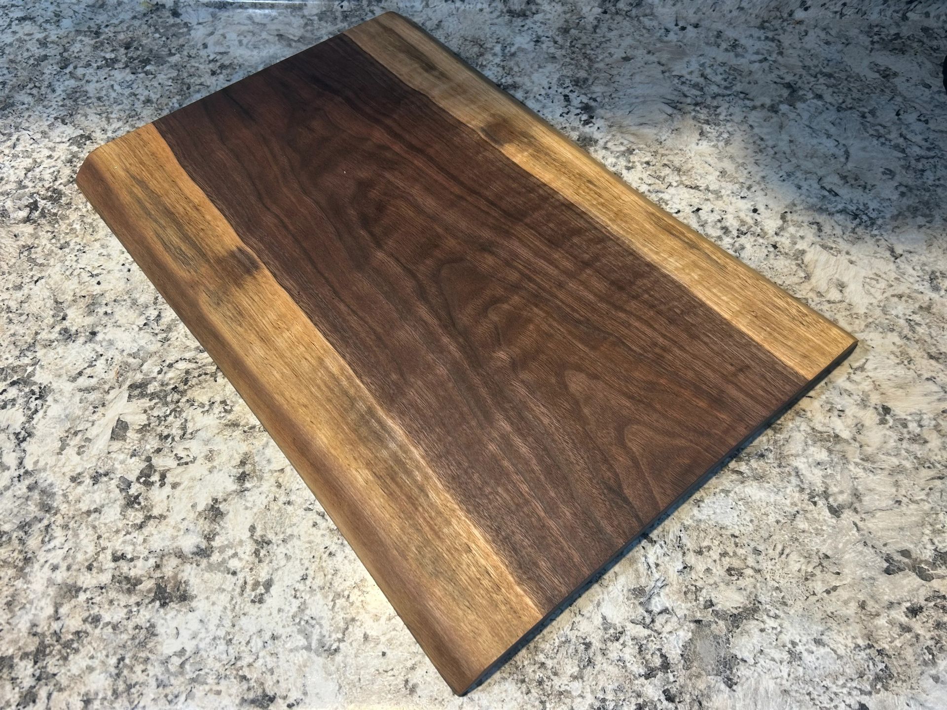 Wooden cutting board on a granite countertop; dark brown center with lighter brown edges.