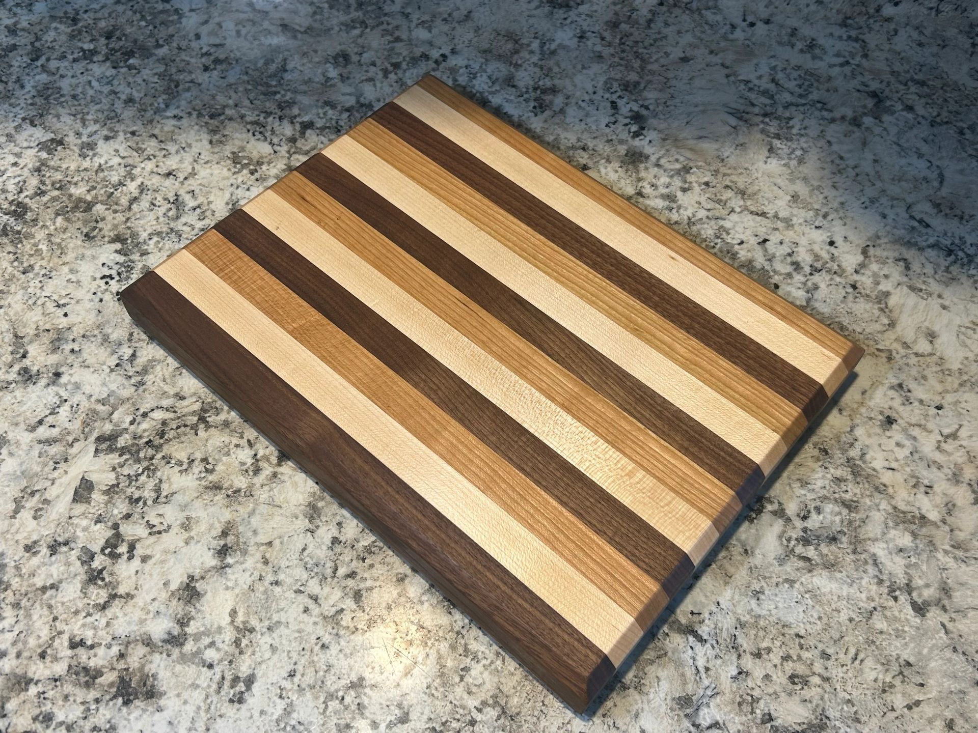 Wooden cutting board with alternating dark and light wood grain stripes, resting on a granite countertop.