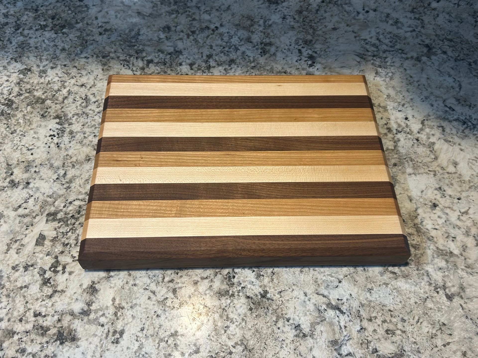 Wooden cutting board with alternating dark and light wood grain stripes, resting on a granite countertop.