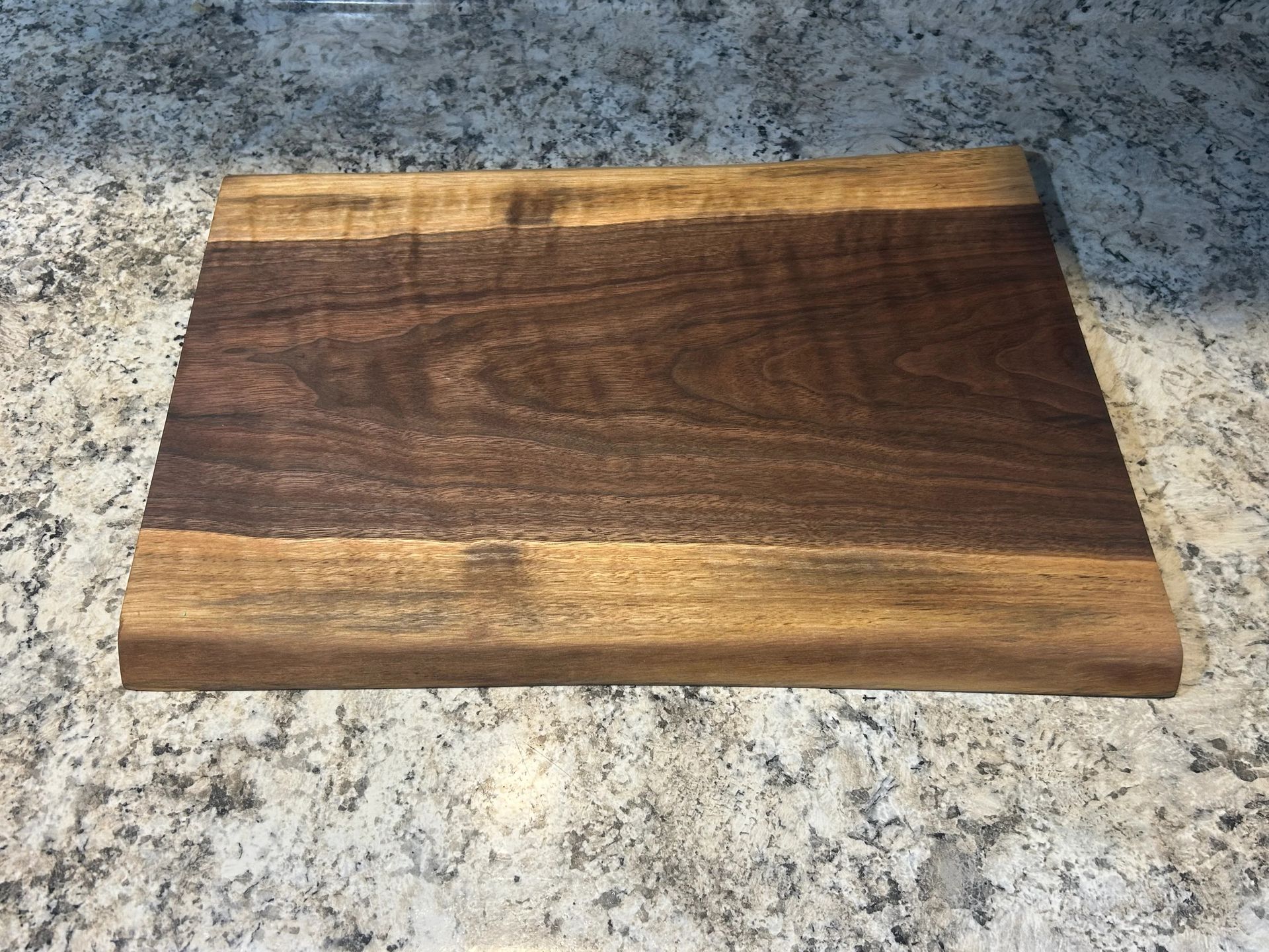 Wooden cutting board on a granite countertop; dark brown center with lighter brown edges.