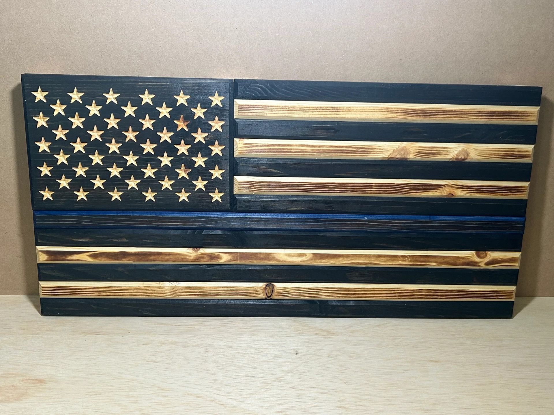 Wooden American flag with a blue line, with charred wood strips.
