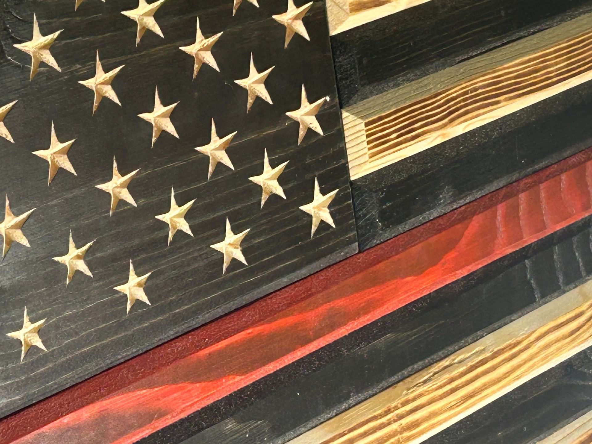 Wooden American flag with a red stripe, likely for firefighters. Black and wood-toned planks.
