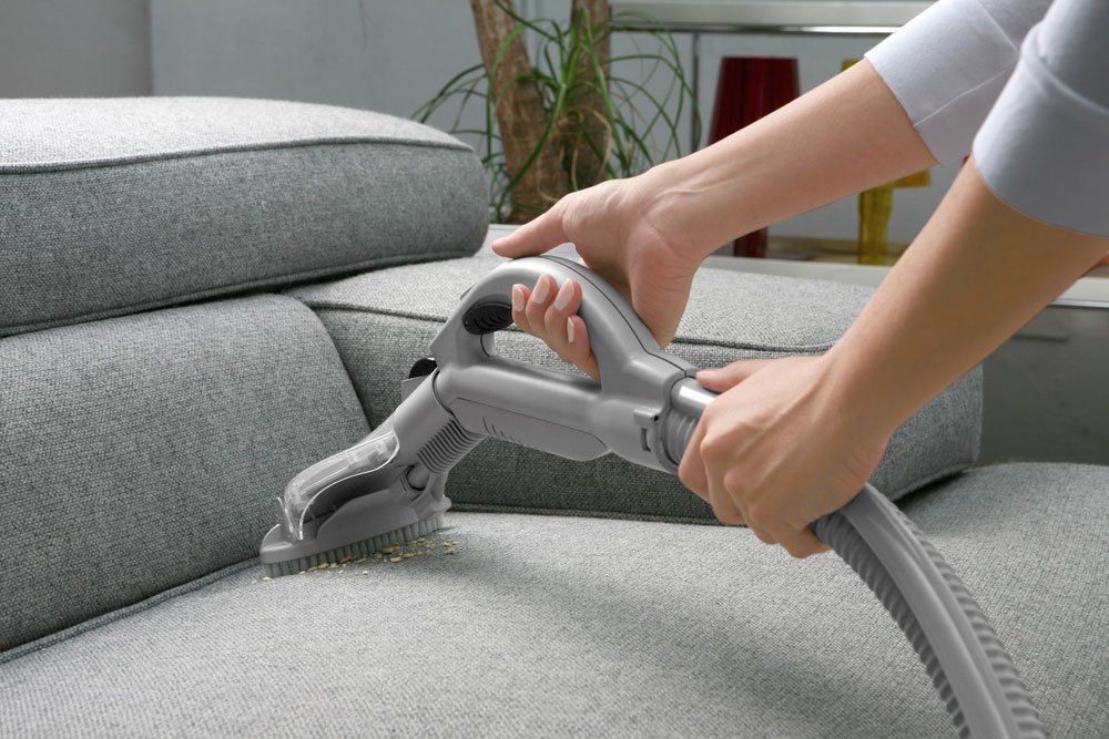 Person Cleaning a Gray Sofa With a Vacuum Cleaner — Enviro Clean Carpet and Tile Cleaning in Umina Beach, NSW