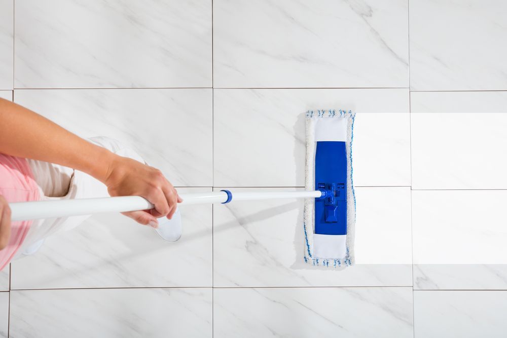 Person mopping white tiled floor with blue mop — Enviro Clean Carpet and Tile Cleaning in Wyong, NSW