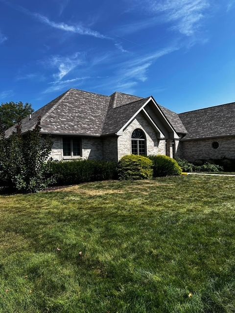 A single-story brick house with a dark gray roof and manicured lawn under a blue sky.
