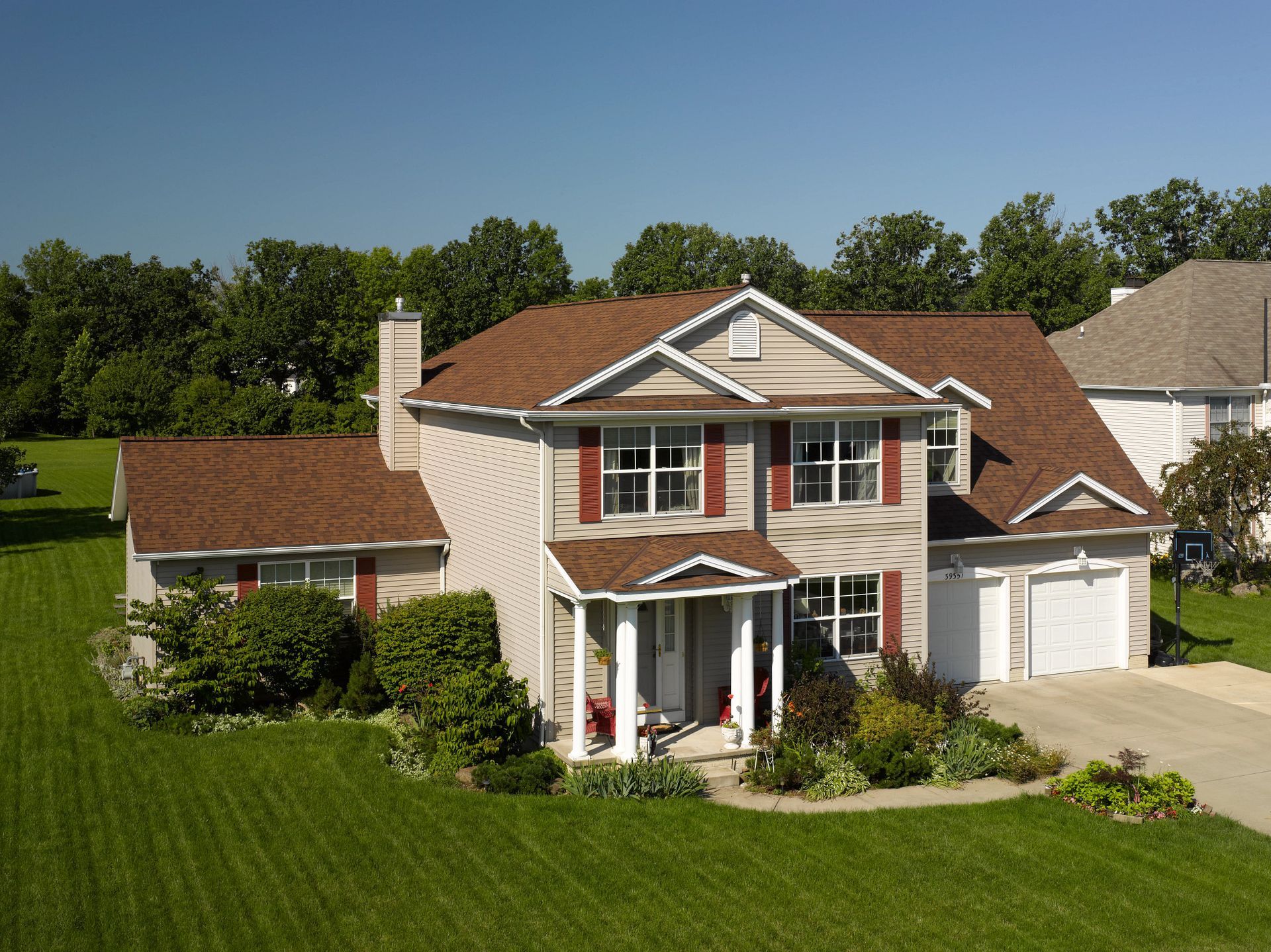 Two-story house with brown roof, red shutters, and a green lawn.