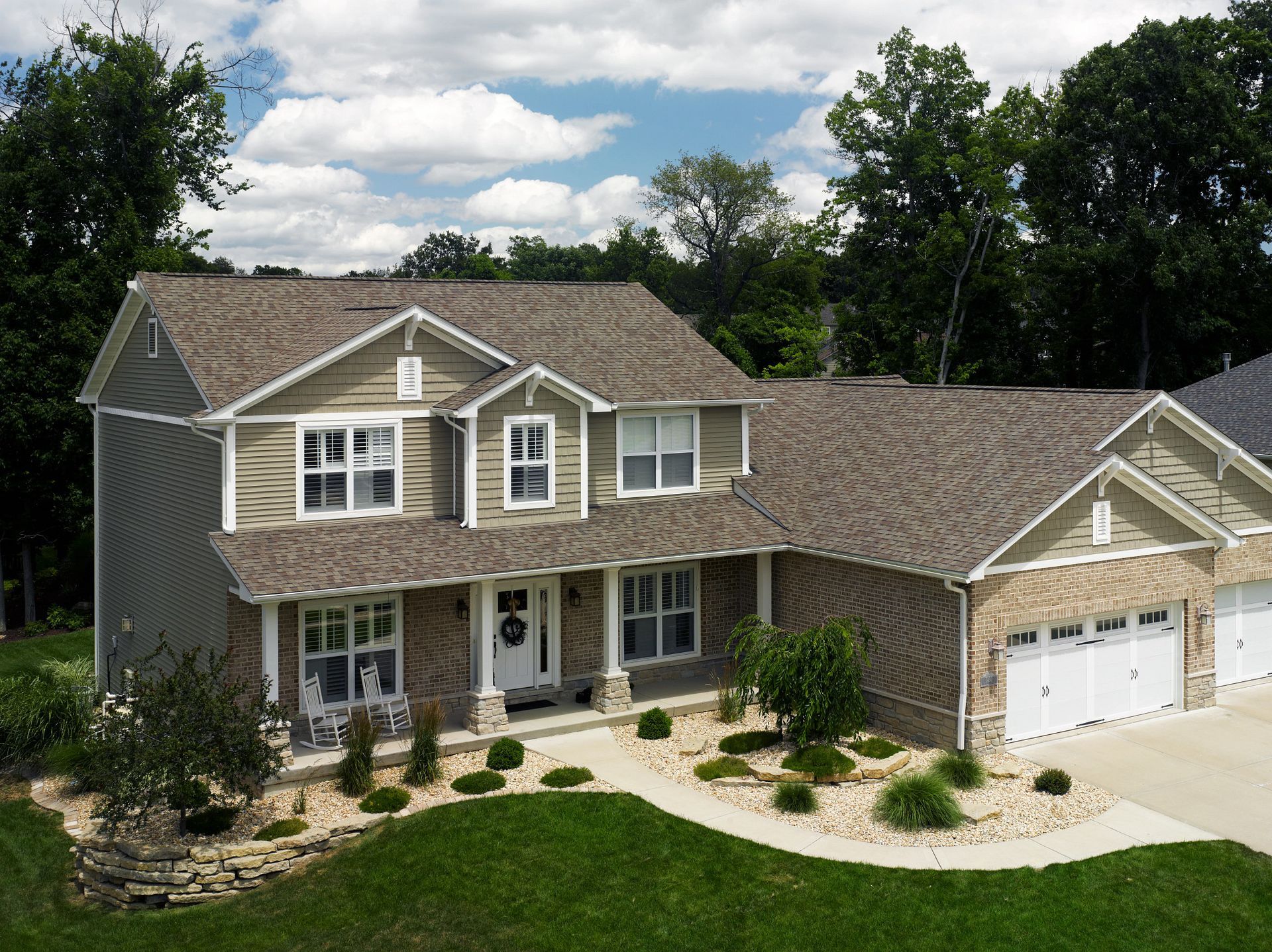 Two-story house with stone facade, green siding, and a three-car garage on a sunny day.