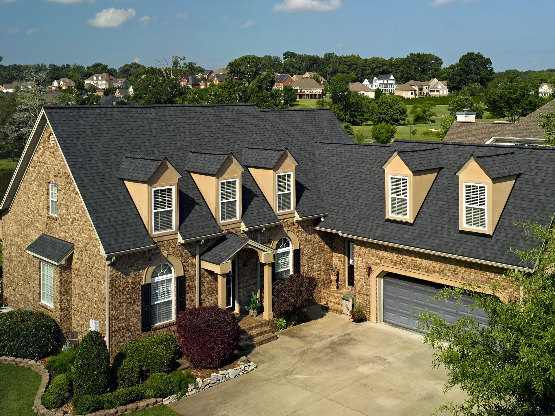 Brick house with dark gray roof, dormers, and garage; front yard landscaping.