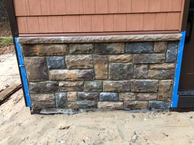 Exterior wall with tan and dark gray stone veneer siding, capped with a stone ledge, bordered by blue painter's tape.