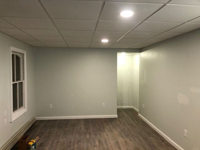 A renovated basement room with light green walls, a white drop ceiling with recessed lights, and wood-look flooring.