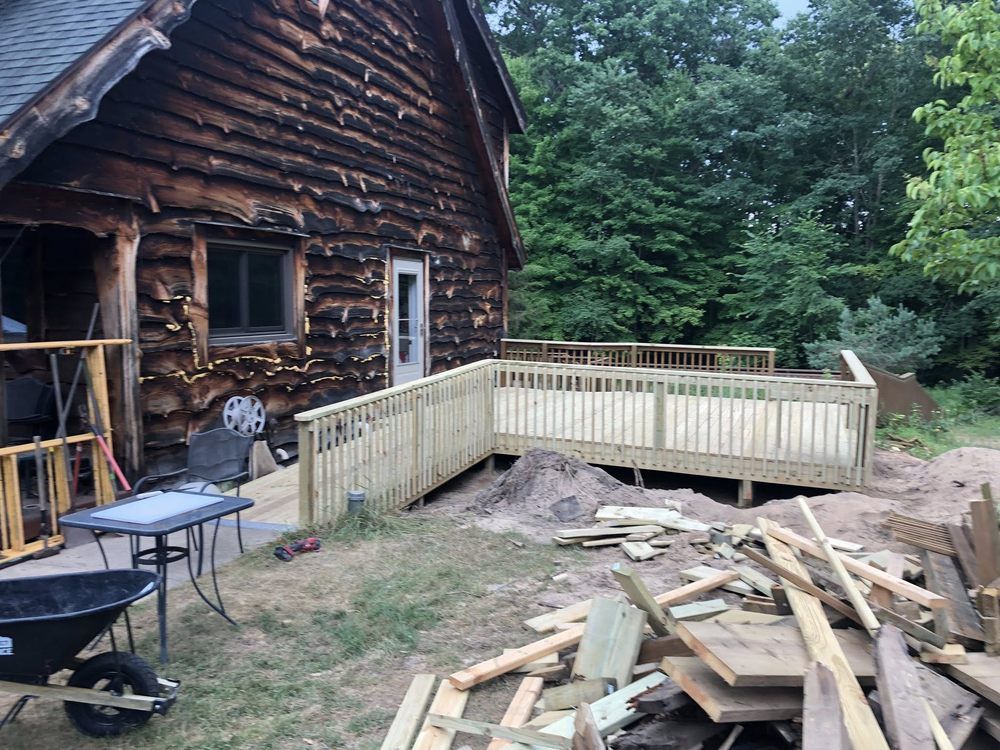 A newly constructed light-colored wooden deck with a wheelchair ramp outside a rustic log cabin under construction.