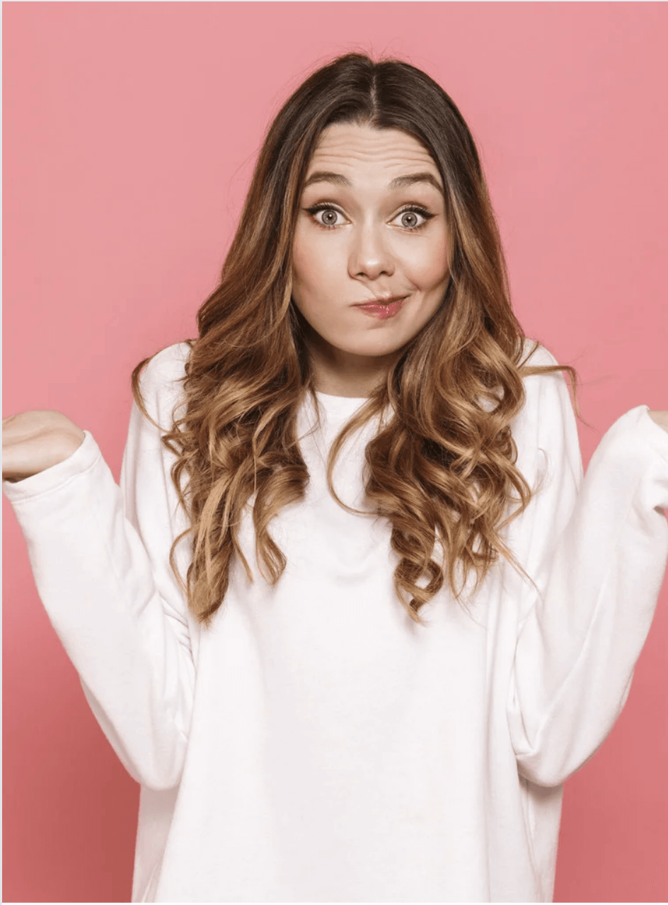 A woman in a white sweater is shrugging her shoulders on a pink background.